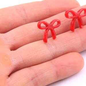 May include: A pair of red bow earrings. The bows are made of a shiny, translucent material.