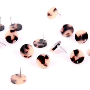 Puede incluir: Una colección de 12 pendientes redondos, con estampado marrón y blanco, con postes plateados. Los pendientes están esparcidos sobre una superficie blanca.