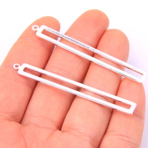 Op de afbeelding: Twee rechthoekige frame hangers van zilverkleurig metaal met een lus aan de bovenkant om op te hangen.