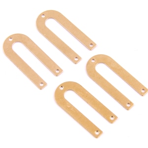 Puede incluir: Cuatro piezas de metal de color dorado en forma de arco con dos agujeros cada una. Las piezas están dispuestas en forma escalonada.