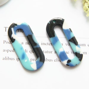 May include: Two oval-shaped, blue, black, and white patterned resin earrings with a hole in the top for hanging.
