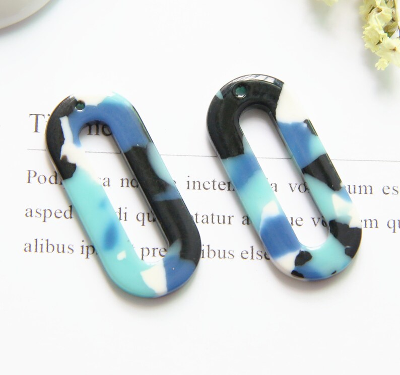 May include: Two oval-shaped, blue, black, and white patterned resin earrings with a hole in the top for hanging.