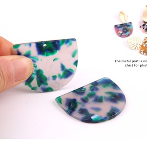 Puede incluir: Dos pendientes de resina en forma de semicírculo con base blanca y patrón marmoleado azul y verde.