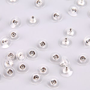 May include: A close-up of a group of silver and clear earring backs. The backs are designed to be used with post earrings.