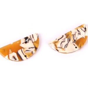 Puede incluir: Dos cuentas de resina en forma de semicírculo con un patrón de mármol blanco, marrón y naranja.