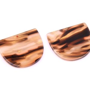 Puede incluir: Dos colgantes de resina de forma semicircular con estampado marrón y blanco con un agujero en la parte superior para encordar.