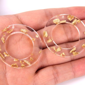 May include: Two clear resin rings with gold flakes embedded inside. The rings have a hole at the top for hanging.