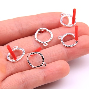 May include: Five silver-toned metal hoops with a textured finish. Each hoop has a small loop at the top and a red plastic tube attached to the loop.