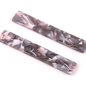 May include: Two long, rectangular, gray and white marbled hair clips.