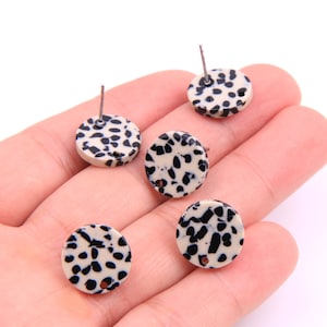 May include: Four round earrings with a black and white dalmatian print. The earrings are made of a white material with black spots.