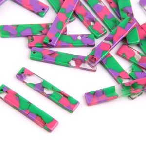 Puede incluir: Un grupo de abalorios rectangulares de acrílico de colores con un patrón de mármol en tonos de verde, rosa y morado. Los abalorios tienen un agujero en cada extremo para sujetarlos a joyas u otras manualidades.