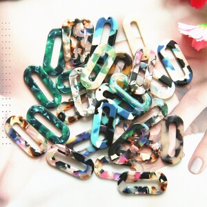May include: Assortment of colorful oval-shaped plastic charms with a hole in the center. The charms have a mottled, marbled pattern in shades of blue, green, pink, and white.