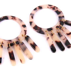 May include: A pair of large earrings with a tortoiseshell pattern. Each earring has a circular hoop with cream, brown, and black markings. Five rectangular charms dangle from each hoop, connected by gold-coloured metal rings, creating a striking accessory.