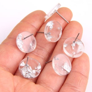 May include: Five clear round resin earrings with silver flakes embedded inside. Each earring has a silver post.