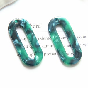 May include: Two green and blue oval-shaped plastic earrings with a hole at the top. The earrings have a marbled pattern.