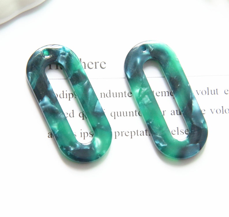 May include: Two green and blue oval-shaped plastic earrings with a hole at the top. The earrings have a marbled pattern.