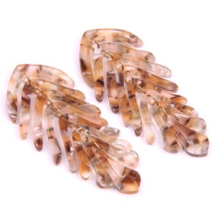 Puede incluir: Un par de pendientes de color marrón y dorado con un diseño de hoja. Los pendientes están hechos de plástico y tienen un aspecto en capas.