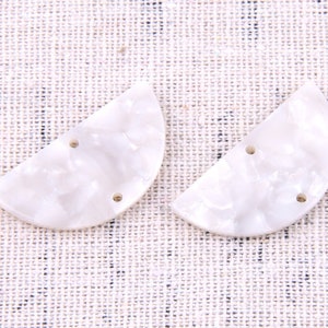 Puede incluir: Dos botones blancos en forma de media luna de concha con una superficie texturizada y tres agujeros cada uno.