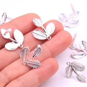 Puede incluir: Encantos de hojas de metal plateado con un bucle para colgar. Los encantos tienen forma de tres hojas conectadas entre sí.