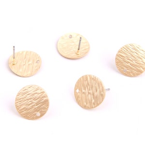 May include: Five gold-colored, round earring studs with a textured surface. Each stud has a post for insertion and a small hole. The earrings are displayed against a white background.