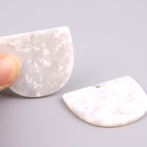 Puede incluir: Dos blancos, semicirculares, colgantes de resina con un agujero en la parte superior para encordar.