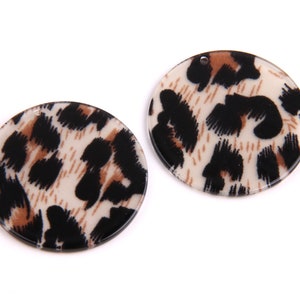 May include: Two round, white, brown, and black leopard print resin embellishments.