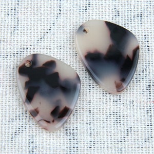 May include: Two white and black patterned resin pendants with a hole for stringing. The pendants are shaped like a teardrop.