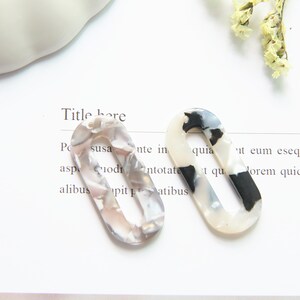 May include: Two oval-shaped hair clips with a marbled pattern in shades of white, black, and gray. The clips have a smooth, glossy finish.