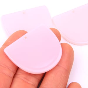 Puede incluir: Tres formas de plástico rosa en forma de semicírculo con un agujero en el centro. Las formas son lisas y tienen un borde ligeramente redondeado.