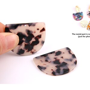 Puede incluir: Dos piezas en blanco de resina en forma de semicírculo, con un patrón de caparazón de tortuga blanco y negro, con un agujero en la parte superior. La parte metálica no está incluida (solo para la foto).