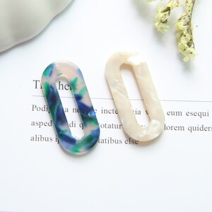 May include: Two oval-shaped hair clips. One is white with a pearlescent finish. The other is blue, green, and white with a marbled pattern.