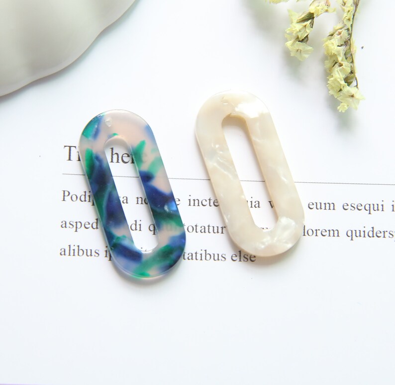 May include: Two oval-shaped hair clips. One is white with a pearlescent finish. The other is blue, green, and white with a marbled pattern.