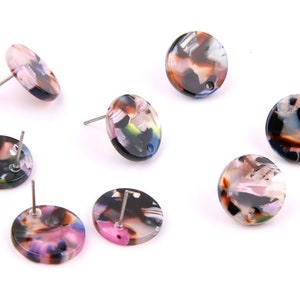 Puede incluir: Seis pares de pendientes redondos de botón coloridos con fondo negro y una variedad de colores, incluyendo rosa, marrón y verde.