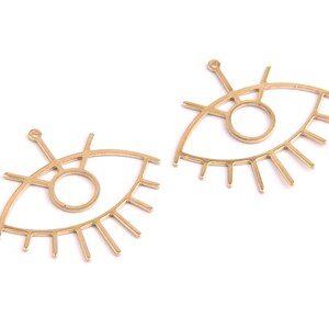 May include: Two gold-colored metal eye charms with a circle in the center and eyelashes around the outside. The charms have a loop at the top for attaching to jewelry.