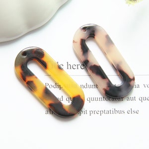 May include: Two oval-shaped, brown, black, and white patterned plastic hair clips with a hole at the top.