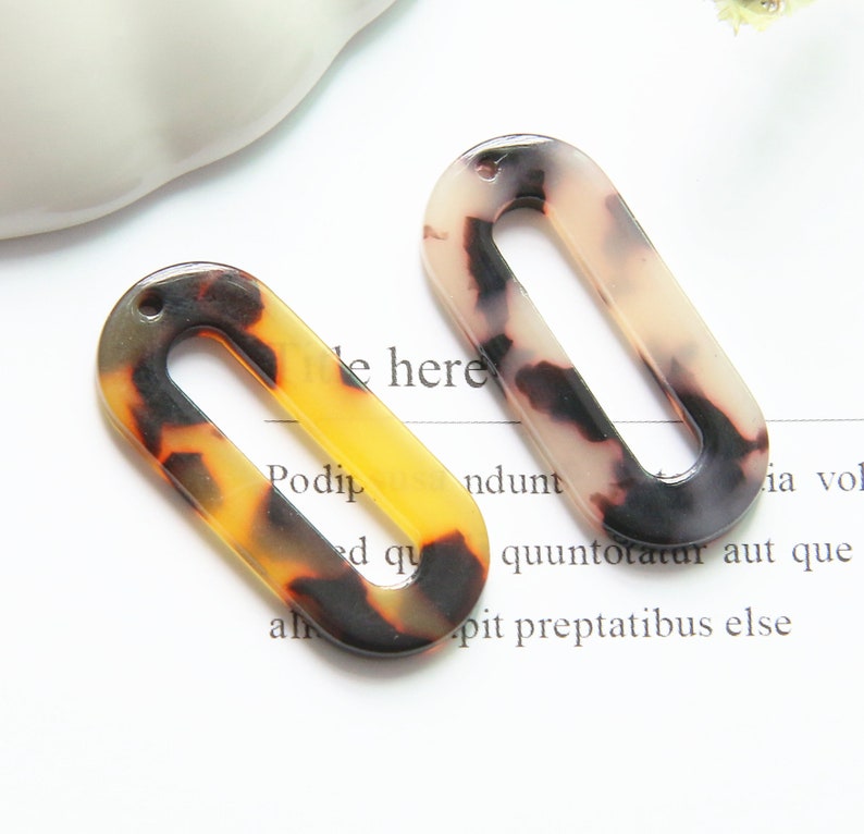 May include: Two oval-shaped, brown, black, and white patterned plastic hair clips with a hole at the top.