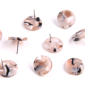 Puede incluir: Ocho pares de pendientes redondos de color crema con vetas negras. Los pendientes tienen postes plateados.