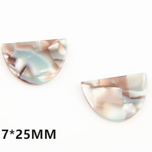 Puede incluir: Dos colgantes de resina en forma de semicírculo con un patrón de mármol en tonos marrones, blancos y azules. Cada colgante tiene un agujero en la parte superior para encordar. Los colgantes miden 17 mm por 25 mm.