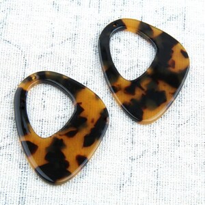 May include: Two brown and black tortoise shell plastic earrings with a large oval cutout in the center.