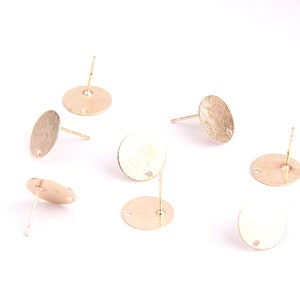 May include: Eight gold-toned earring blanks with a round shape and a small hole in the center. Each blank has a post attached to the back.