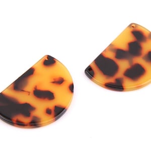 Puede incluir: Dos pendientes de resina con forma de semicírculo y estampado de caparazón de tortuga. Los pendientes son de color marrón claro con manchas marrones oscuras.