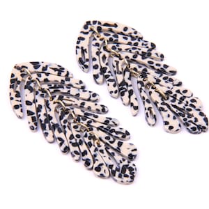 Könnte beinhalten: Ein Paar lange, schwarz-weiße gemusterte Ohrringe. Die Ohrringe sind aus einem leichten Material gefertigt und haben ein baumelndes Design.