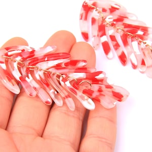 Puede incluir: Un par de pendientes de declaración rojos y blancos con un diseño geométrico. Los pendientes están hechos de plástico y tienen una forma colgante.