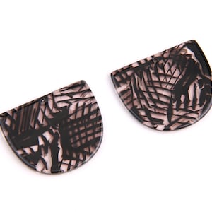 Könnte beinhalten: Zwei halbkreisförmige Formen aus Harz mit schwarz-weißem Muster und einem Loch oben. Die Formen sind durchscheinend und haben einen hellbraunen Hintergrund.