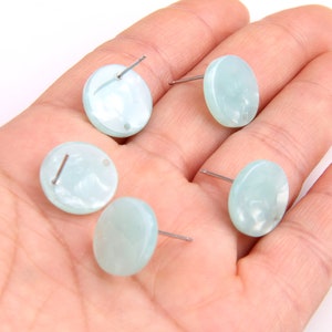 Puede incluir: Cuatro pendientes redondos de color azul claro con postes plateados. Los pendientes están hechos de un material nacarado.