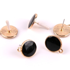 Puede incluir: Cuatro pendientes de botón dorados con tapas redondas de esmalte negro. Los respaldos de los pendientes son visibles.