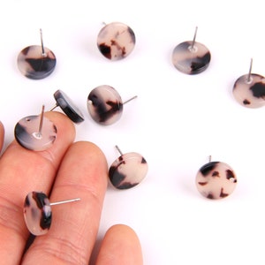 Puede incluir: Un conjunto de ocho pendientes redondos con estampado blanco y negro y postes plateados. Los pendientes tienen un diámetro de aproximadamente 1 cm.