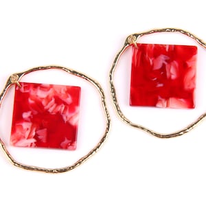 May include: A pair of gold hoop earrings with red and white marbled square accents.