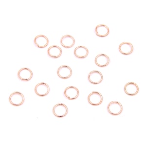 Könnte beinhalten: Eine Sammlung von 18 goldfarbenen Sprungringen, verstreut auf weißem Hintergrund. Diese Ringe werden häufig in der Schmuckherstellung und im Handwerk verwendet.