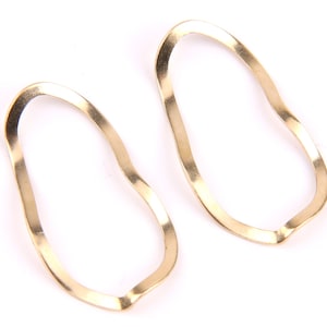 Puede incluir: Un par de pendientes de aro abierto ondulados de color dorado. Los pendientes están hechos de metal y tienen una forma orgánica única.